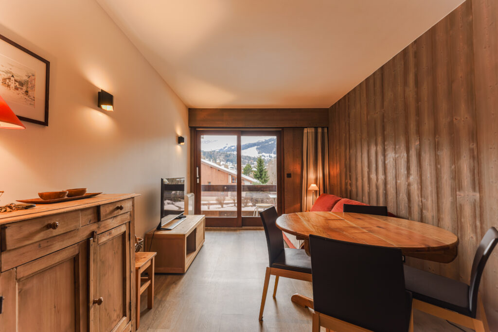 Pièce de vie lumineuse et chaleureuse avec canapé convertible et accès direct au balcon, Megève. Espace salle à manger convivial pour 4 personnes dans un appartement de standing au Jaillet.