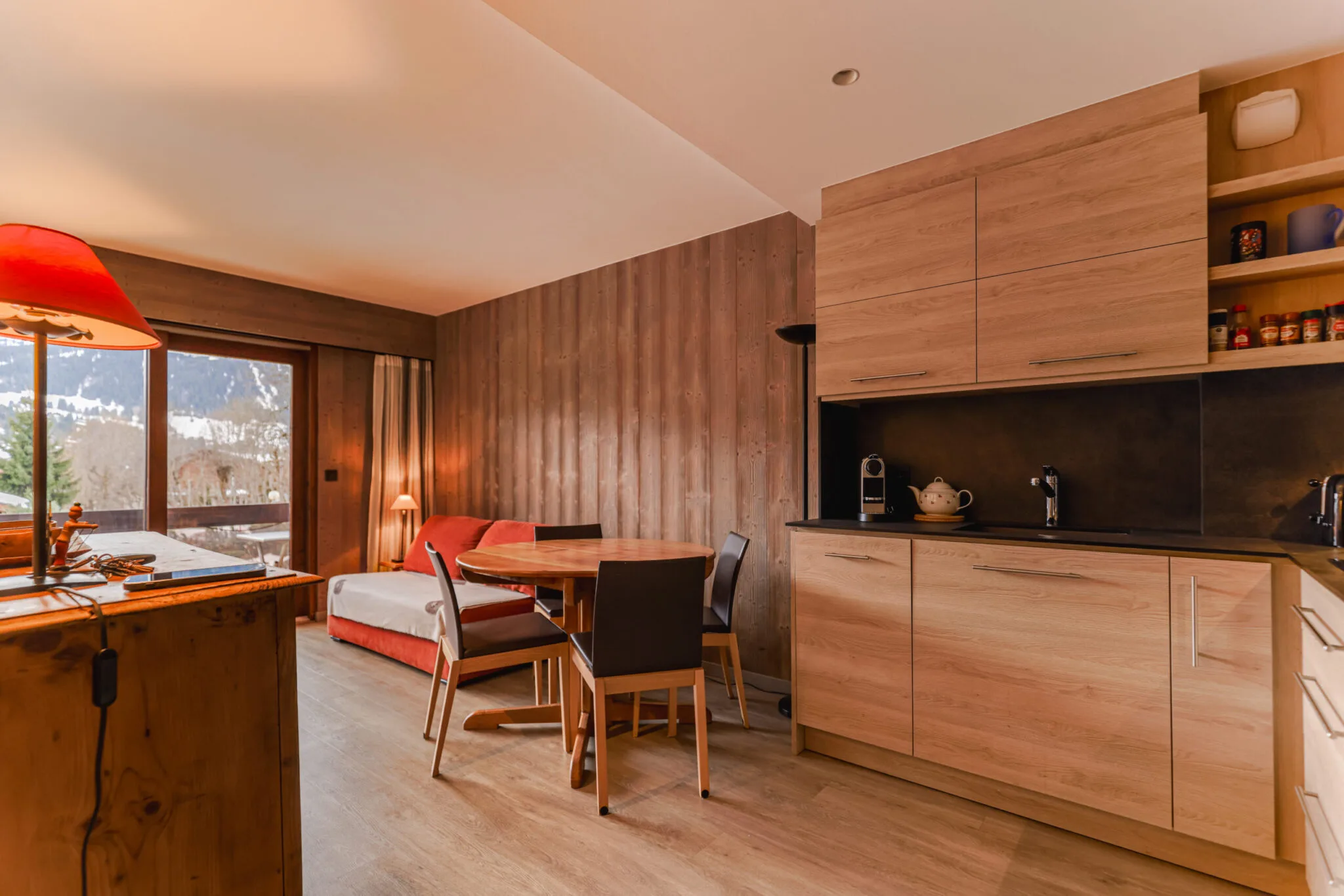 Pièce de vie lumineuse et chaleureuse avec canapé convertible et accès direct au balcon, Megève. Espace salle à manger convivial pour 4 personnes dans un appartement de standing au Jaillet.