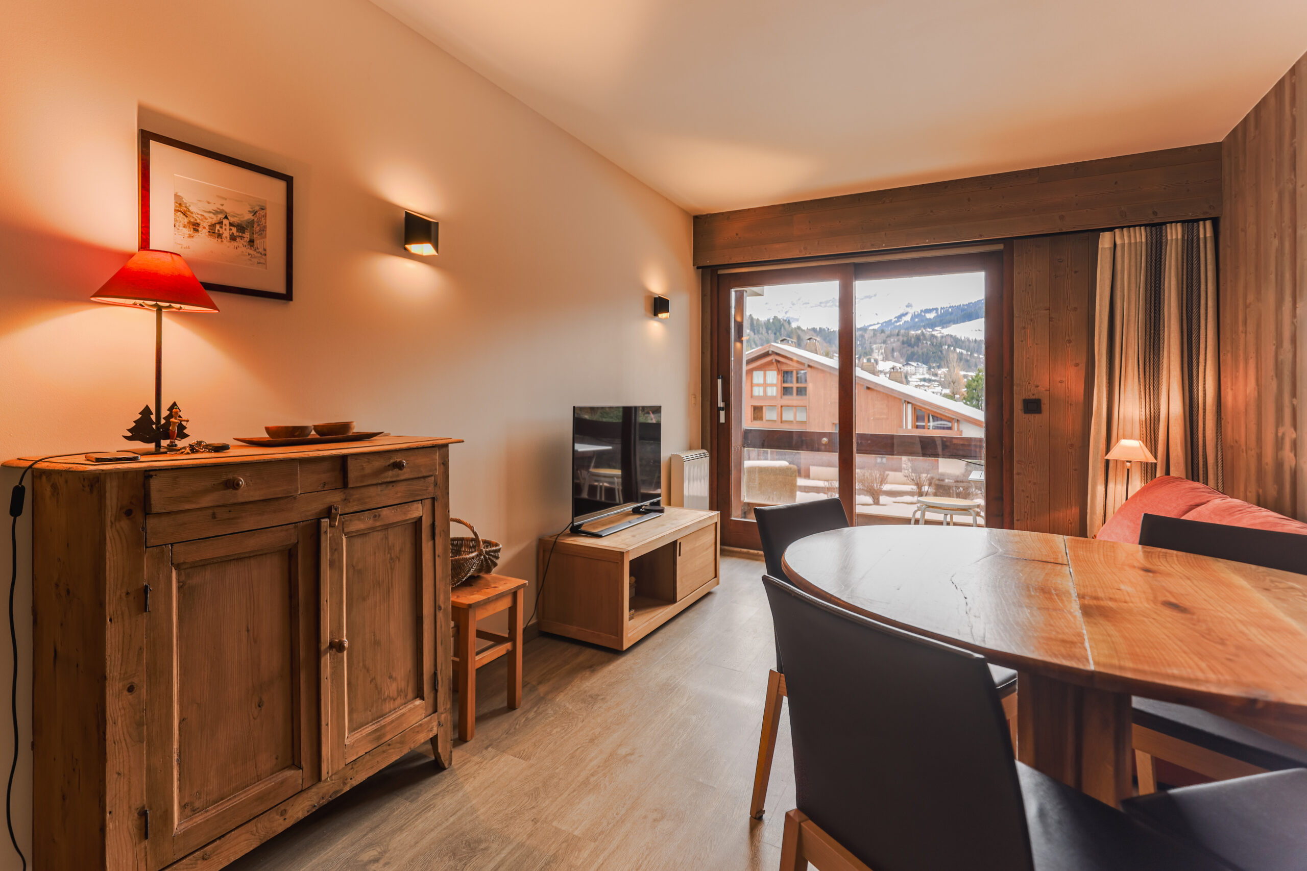 Pièce de vie lumineuse et chaleureuse avec canapé convertible et accès direct au balcon, Megève. Espace salle à manger convivial pour 4 personnes dans un appartement de standing au Jaillet.